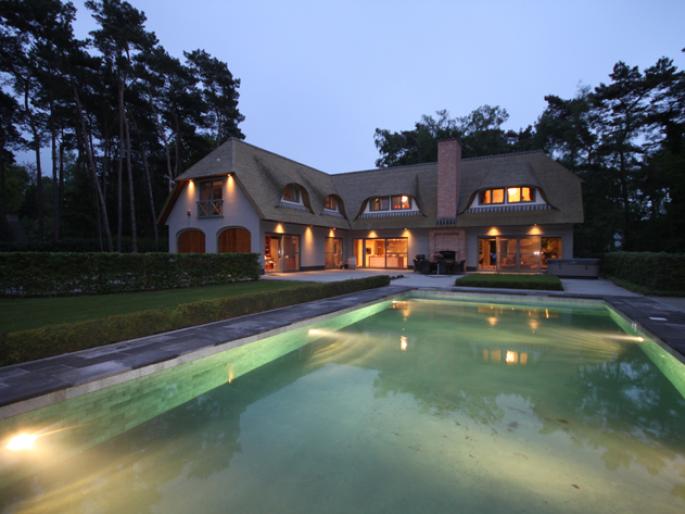 View of a well-lit villa and swimming pool at dusk in Keerbergen